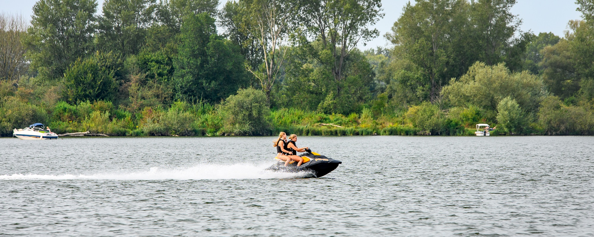 Twee personen op een waterscooter op de Maasplassen in Hart van Limburg, een populair gebied om te watersporten, met groene oevers en recreatieboten.