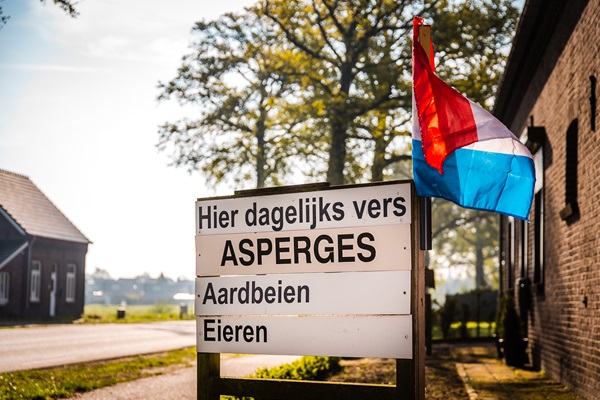 Bord met daarop de Limburgse streekproducten zoals asperges die er te koop zijn onder een wapperende Nederlandse vlag