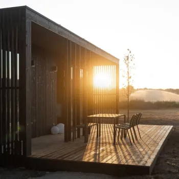 Donkerhouten lodge van Eco by Nature in Heythuysen met een ruim houten terras, zitje en uitzicht op de natuur bij zonsondergang.